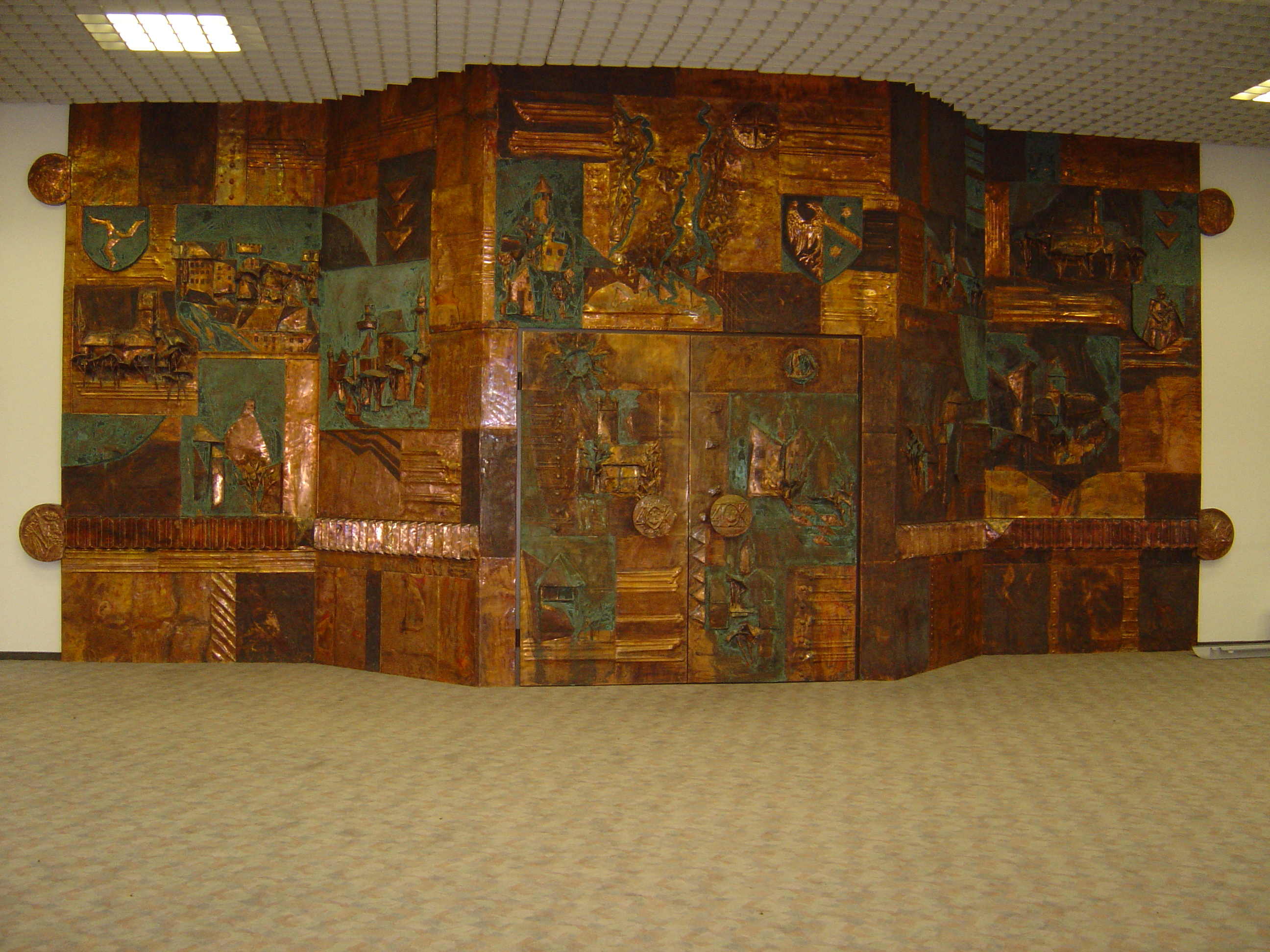 Das Bild zeigt die von Arnulf Heimhofer gestaltete Eingangshalle der ehemalige AOK Kaufbeuren. Es handelt sich dabei um eine Kupferarbeit mit farblicher Bearbeitung.